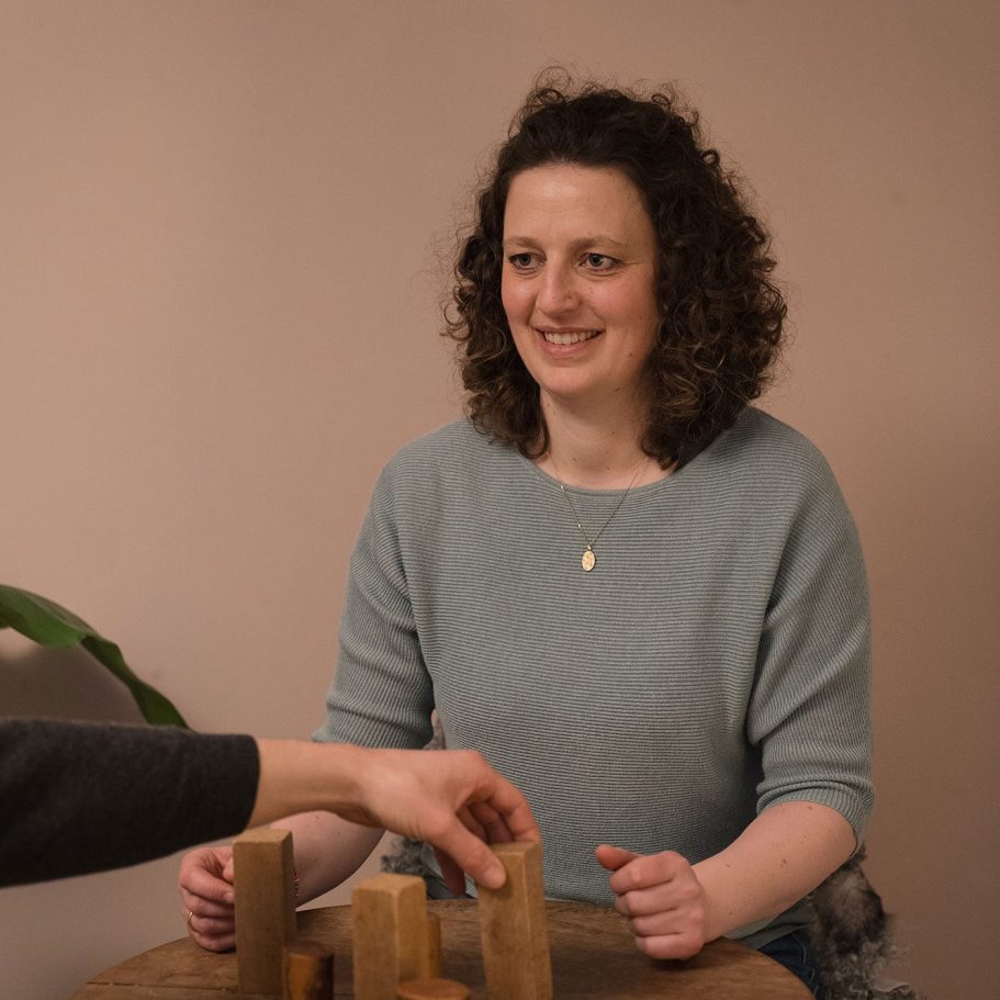 Eine Frau mit lockigem Haar sitzt an einem Tisch und betrachtet Holzklötze.