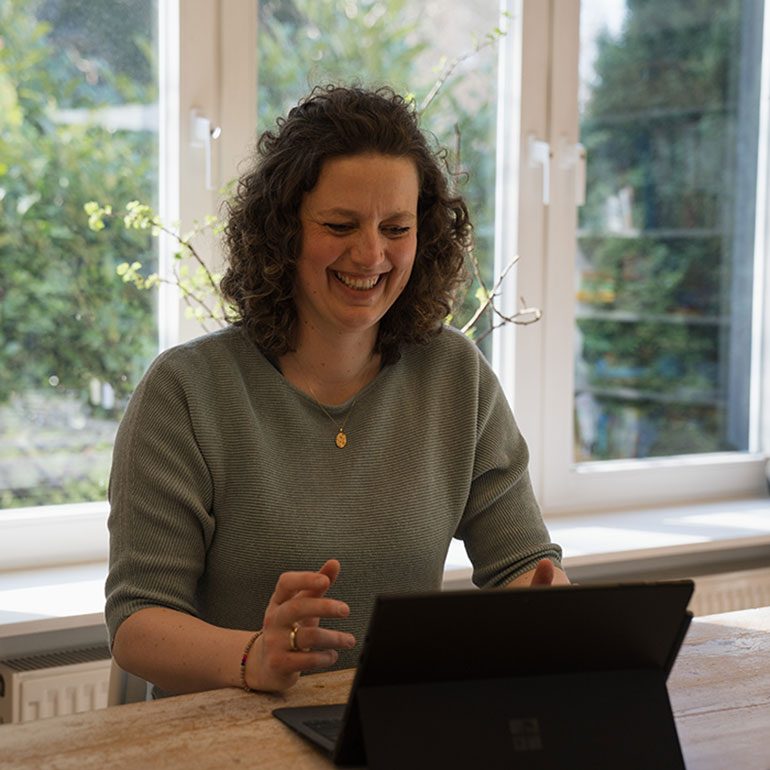 Frau mit lockigem Haar lächelt, während sie an einem Laptop sitzt.
