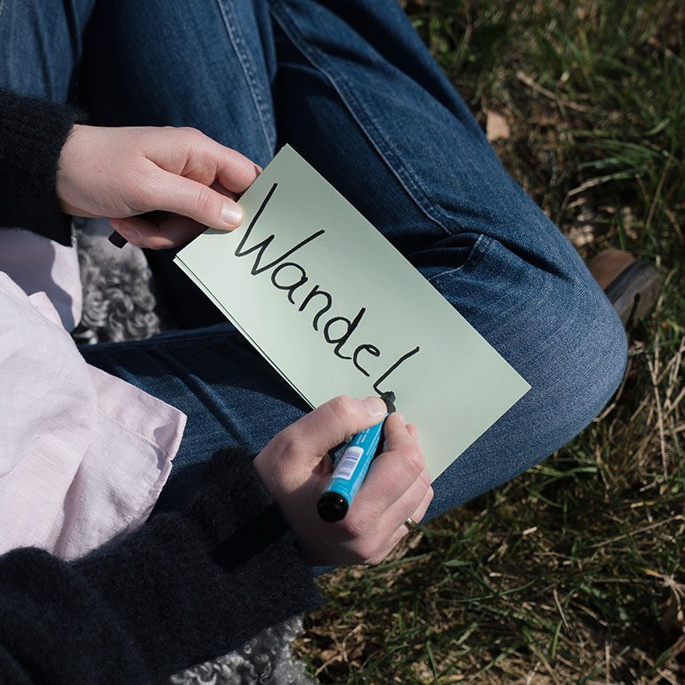 Eine Person hält eine grüne Karte mit dem Wort "Wandeln" in der Hand.