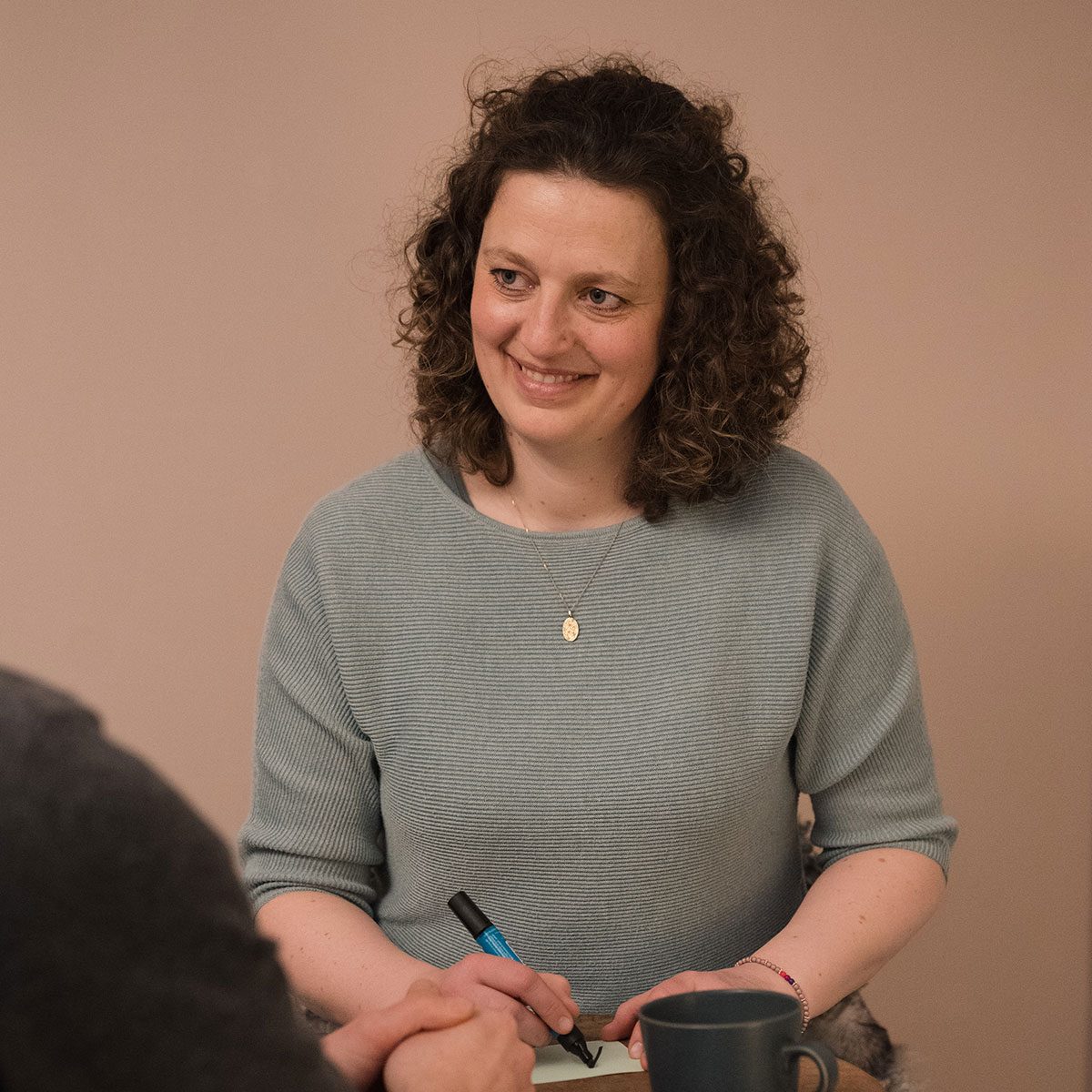 Lächelnde Therapeutin mit Locken, die Notizen macht und einen Stift hält.