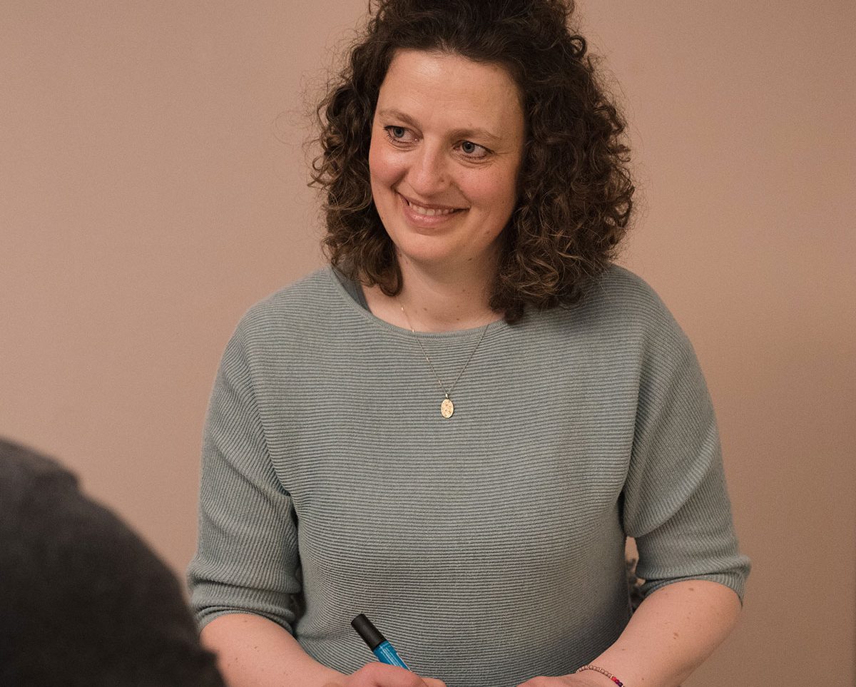 Beraterin mit lockigem Haar, lächelt und hält einen Stift in der Hand.